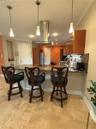 Kitchen featuring an expansive stone countertop, stainless steel ceiling-mounted vent hood, natural stone tile flooring, three pendant lights, and woo