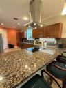Kitchen featuring a stone-surface island, stainless steel chimney-style range hood, recessed lighting, wood cabinetry, and under-cabinet lighting