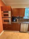 Kitchen featuring wood cabinetry, stone countertops, stainless steel double wall oven, stainless steel dishwasher, and large-format tile flooring