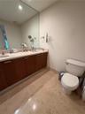 Dual-sink vanity with wood-finish cabinetry, solid surface countertop, expansive wall-to-wall mirror, and neutral tile flooring