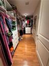 Walk-in closet featuring wood-finish flooring, built-in floor-to-ceiling shelving units, and integrated white cabinetry with multi-drawer storage