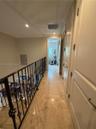 Hallway featuring stone-finish tile flooring, decorative wrought-iron railings, recessed lighting, and multi-panel doors with metallic hardware