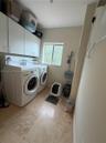 Laundry area featuring wall-mounted upper cabinetry, neutral stone-finish tile flooring, and a window providing natural light