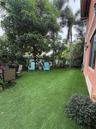 Private outdoor space featuring synthetic lawn, mature perimeter trees, established shrubbery, and metal fencing