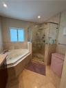 Jetted soaking tub and walk-in shower with a glass enclosure and wall-mounted rainfall showerhead, complemented by neutral-toned stone tile flooring a