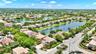 Aerial perspective featuring a multi-story residence with a concrete tile roof, paver driveway, integrated multi-car garage, and lush perimeter landsc