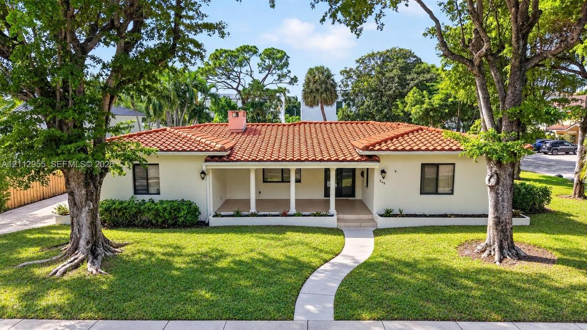 Single-story residence featuring a tile roof, covered front porch, stucco exterior, mature trees, and a manicured lawn