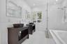 Bathroom featuring dual dark wood vanities with vessel sinks, a glass-enclosed shower, a deep soaking tub, and plantation shutters