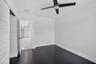 Room featuring dark wood-finish flooring, a multi-blade ceiling fan with integrated lighting, and a solid-core interior door