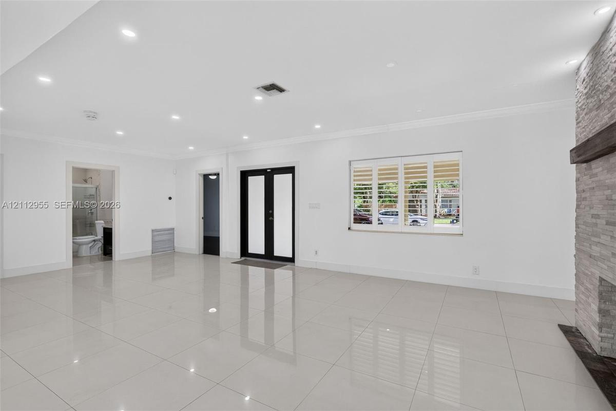 Large-format tile flooring, recessed ceiling lighting, stone-clad fireplace with a timber mantel, double-entry front door with glass insets, and windo