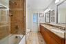 Bathroom featuring a dual-sink vanity with stone countertops, wood cabinetry, tile flooring with decorative inlay, and a glass-enclosed shower and tub