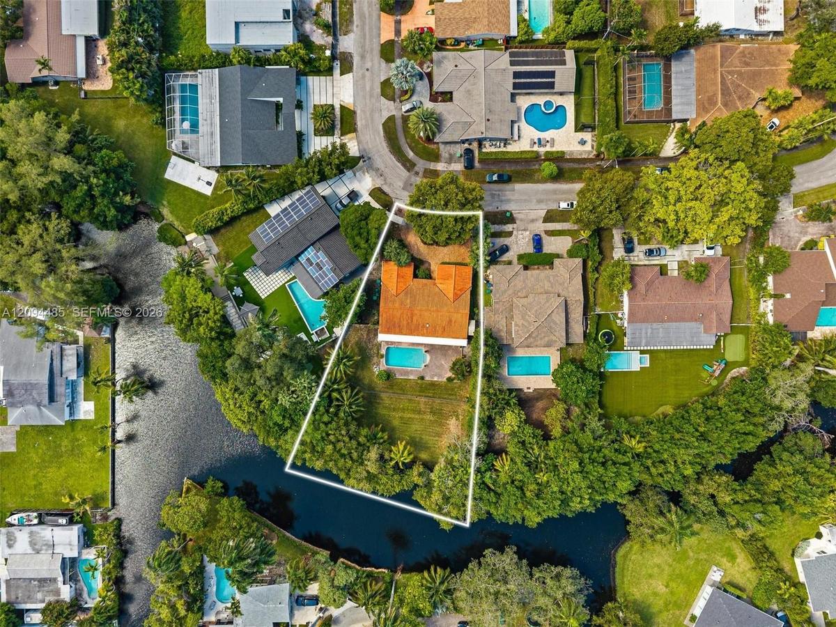 Aerial perspective of a waterfront property featuring a terracotta-tiled roof, a private swimming pool, and an expansive rear lawn area situated along