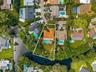 Aerial perspective of a waterfront property featuring a terracotta-tiled roof, a private swimming pool, and an expansive rear lawn area situated along