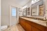 Dual-sink vanity featuring wood-finish cabinetry, stone countertops, integrated oval basins, and framed wall mirrors