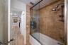Shower-tub combination featuring floor-to-ceiling tile surround with decorative inlay, glass sliding shower door, recessed wall niche, and metal hardw