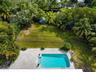 Outdoor living space featuring an in-ground swimming pool, concrete paver patio, metal perimeter fencing, manicured lawn, and mature tropical landscap