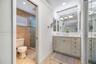 Vanity featuring a white countertop with an integrated basin, shaker-style cabinetry with metallic hardware, large-format wall mirror, and natural sto
