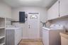 Laundry area featuring wood-finish flooring, white upper wall-mounted cabinetry, integrated shelving, and a utility sink
