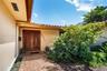 Stucco exterior entry featuring a herringbone-patterned brick walkway, double wood-paneled doors with metallic hardware, and a terracotta tile roof ed