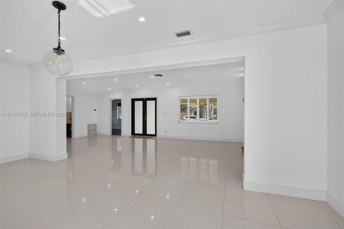 Open-concept interior featuring large-format porcelain tile flooring, crown molding, recessed lighting, double entry doors, and a decorative glass pen