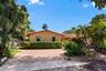Single-story residence featuring a terracotta-tiled roof, brick-paved driveway, and lush tropical landscaping