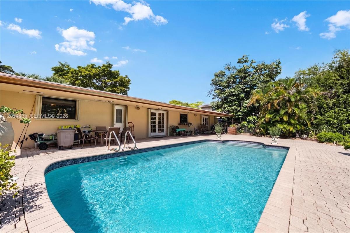 In-ground swimming pool with masonry paver surround, expansive patio, and mature landscaping