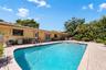 In-ground swimming pool with masonry paver surround, expansive patio, and mature landscaping