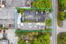 Aerial perspective of the property featuring a paved asphalt parking area, designated parking stalls, mature perimeter landscaping, and established tr