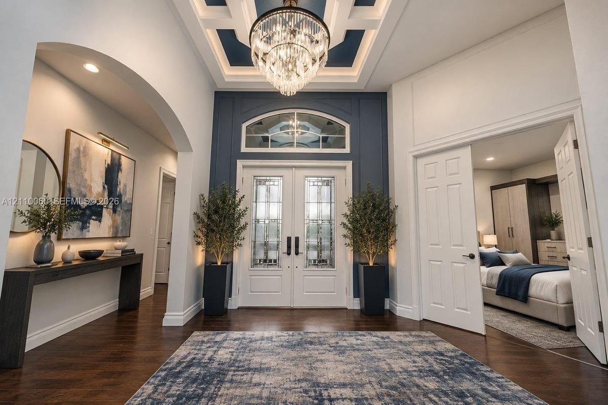 Virtually staged. Foyer featuring wood-finish flooring, a coffered ceiling with a crystal chandelier, arched entryway, and double entry doors with dec