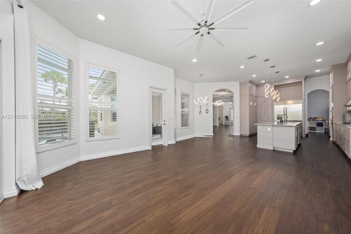 Open floor plan featuring wood-finish flooring, multi-pane windows with plantation shutters, an expansive kitchen island with a neutral countertop, re
