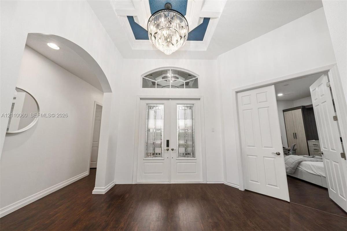 Foyer featuring double entry doors with decorative glass inserts, a recessed tray ceiling with accent color, a crystal chandelier, arched architectura