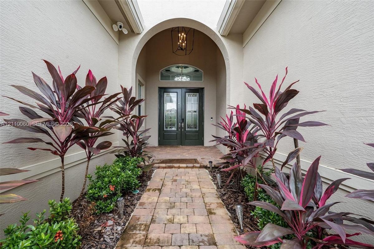 Arched entryway featuring a paver walkway, double-door entry with arched transom window, built-in geometric lantern-style lighting, and mature landsca