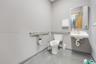 Restroom featuring a wall-mounted vitreous china sink, stainless steel grab bars, a rectangular mirror with a metal frame, and a wall-mounted paper di