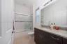 Bathroom featuring dark wood-finish cabinetry, a stone-patterned countertop, an integrated sink, a full-width vanity mirror, and a tub-shower combinat