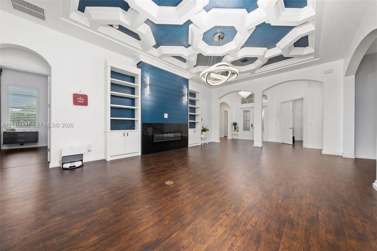 Geometric coffered ceiling with inset blue accents, wood-finish flooring, built-in floor-to-ceiling cabinetry, shiplap fireplace surround, and modern 