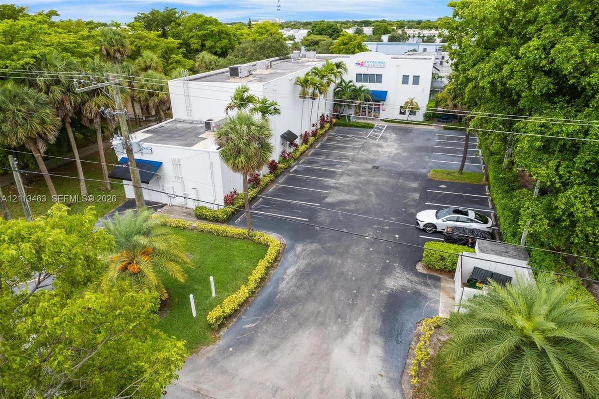 Multi-story commercial building featuring a dedicated asphalt parking lot, manicured lawn areas, established palm trees, and perimeter landscaping