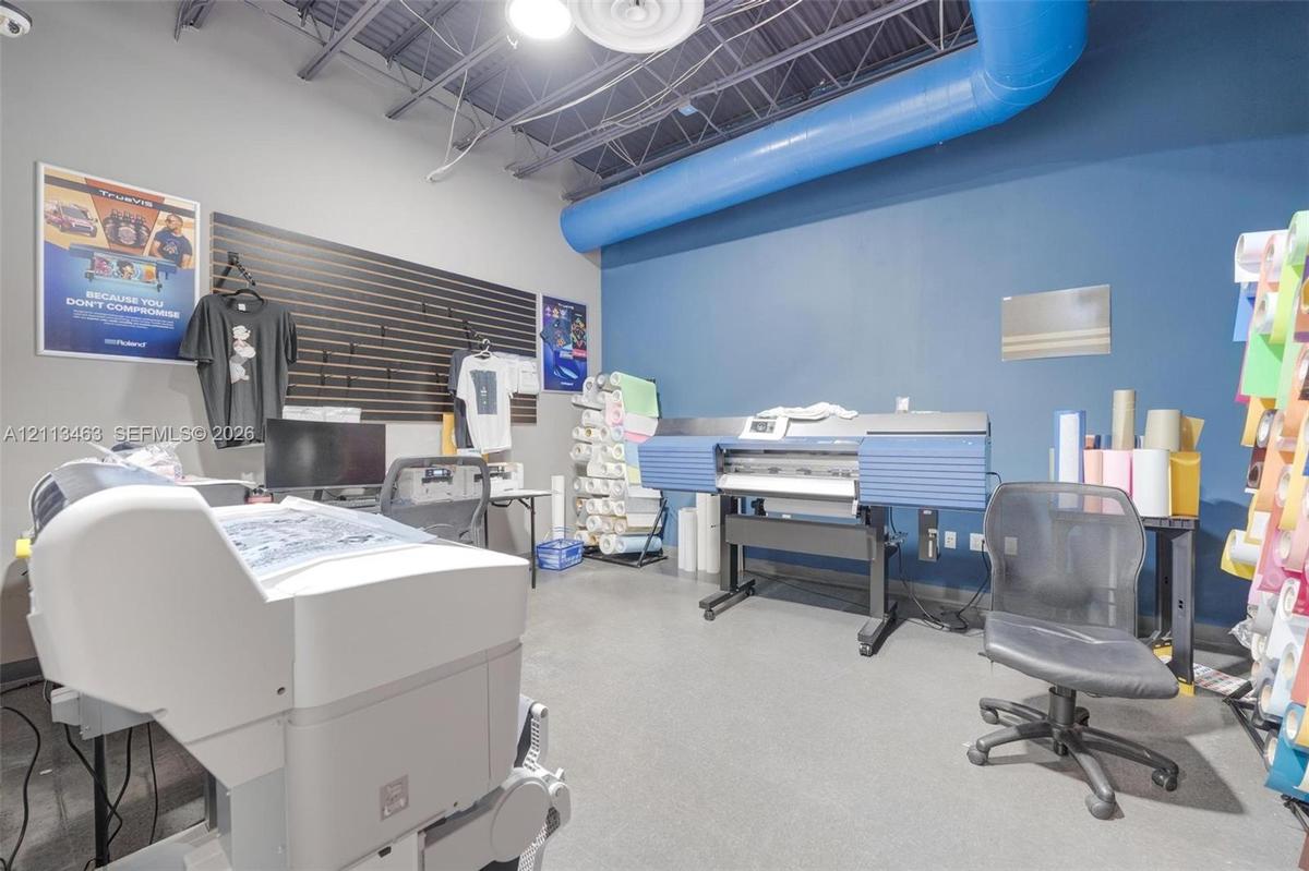 Industrial-style workspace featuring exposed ceiling joists, blue exposed ductwork, concrete flooring, and horizontal slat wall paneling