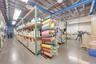 Industrial workspace featuring high-clearance ceilings with exposed ductwork, concrete flooring, overhead linear lighting, and heavy-duty steel pallet