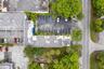 Aerial perspective featuring an L-shaped structure, paved parking area with marked spaces, and established landscaping with mature trees