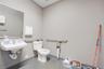 Wall-mounted porcelain sink with chrome fixtures, large rectangular mirror, dual stainless steel support grab bars, and low-profile toilet