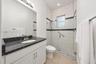 Bathroom featuring a white vanity cabinet with a dark stone countertop, an integrated sink with a chrome faucet, a walk-in shower with a glass enclosu