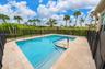 In-ground pool with built-in stairs, tan stone paver decking, black mesh safety fencing, and mature palm tree landscaping