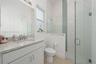 Bathroom featuring a vanity with stone-finish countertop and undermount sink, large wall-mounted mirror, walk-in shower with glass enclosure, vertical