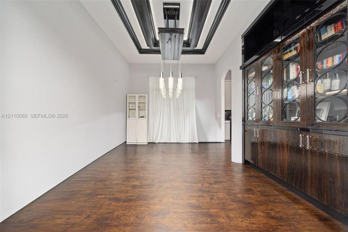 Wood-finish flooring, dramatic coffered ceiling with black detailing, built-in floor-to-ceiling cabinetry with glass-panel doors, and an elongated mul