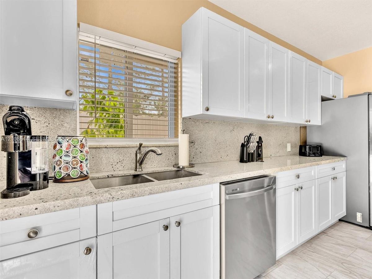 Kitchen featuring white shaker-style cabinetry, stone-finish countertops, stainless steel undermount sink with arched faucet, stainless steel dishwash