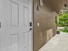 White four-panel entry door with electronic keypad lock, textured stucco exterior, and covered concrete walkway