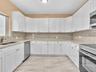 Kitchen featuring white shaker-style cabinetry, stone countertops, integrated stainless steel appliances, and large-format tile flooring
