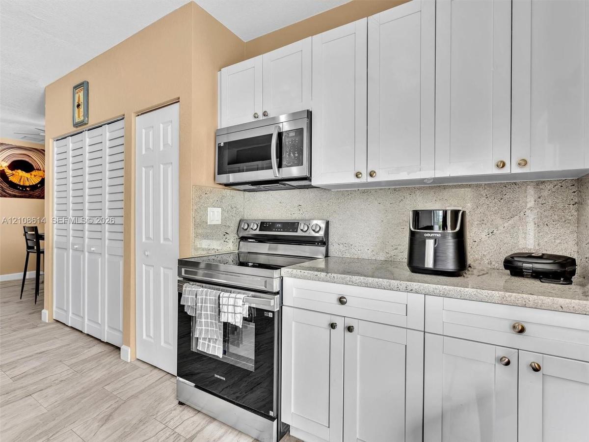 Kitchen featuring white shaker-style cabinetry, stone-finish countertops, stainless steel appliances, and wood-finish flooring