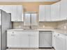 Kitchen featuring white shaker-style cabinetry, stone-surface countertops, stone backsplash, stainless steel dishwasher, and a dual-basin sink with a 