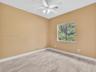 Neutral-toned interior space featuring wood-finish flooring, a white ceiling fan with integrated lighting, and a window with exterior greenery